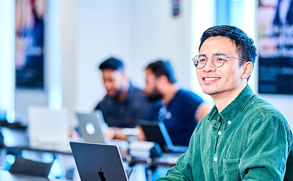 A student sat in front of a laptop smiling